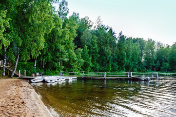 Fototapeta na wymiar A quiet pier on the sandy shore of a forest lake with moored boats white