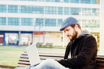 Young man sitting on bench with laptop on his lap.