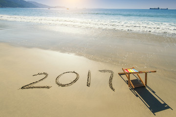 Fototapeta na wymiar 2017 written in sand write on tropical beach with Deck chair.