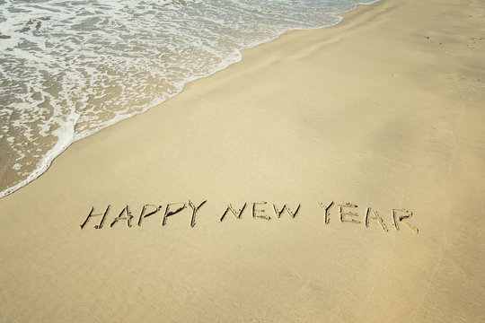 happy new year written in sand write on tropical beach