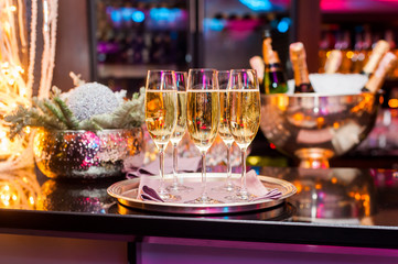 Glasses of champagne .New Year mood/Glasses of champagne on tray in restaurant on the background of Christmas decorations and bottle of champagne.Selective focus