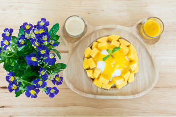 Bingsu ( Korea food) mango served with sweetened condensed milk and flowers vase on table