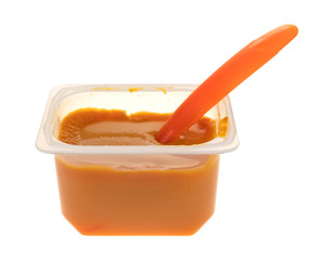 Baby food in a plastic container with a spoon inserted into the food isolated on a white background.