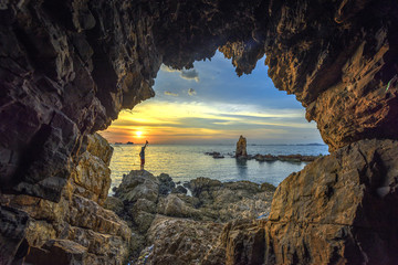 Man looking Rock standing alone, view from cave at sunset