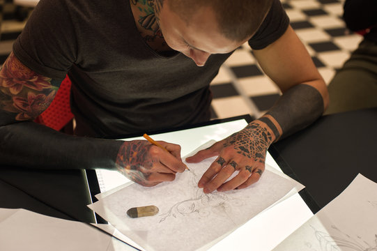 Young male tattoo artist creating sketch in parlor