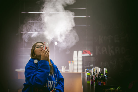 young Cute woman, the seller in vape shop shop, smoking electronic cigarette,  vaping and releases a cloud of vapor and inflates soap bubbles