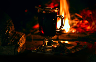 evening by the fireplace. Burning fire, cozy warm atmosphere at home. Glass with mulled wine. Dark photo.

