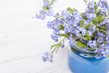 small blue flowers in a jar on a white wooden background