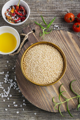 Light cereal quinoa in a metal bowl on  simple wooden background with tomatoes, rosemary, olive oil and salt. Top view