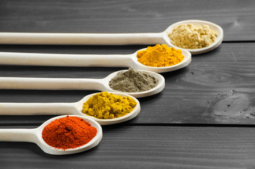 Dry powder spices in wooden mixing spoons at the table