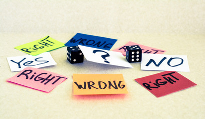 Around black dice are small pieces of paper. On pieces of paper written words and a question mark.
