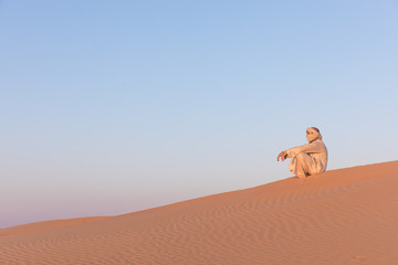 Man in a traditional arab dress in desert at sunrise. Dubai, UAE.