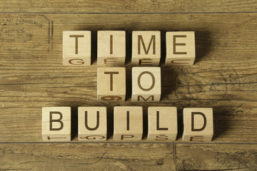 time to build text on wooden cubes on a wooden background