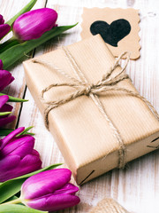 Gift box and tulips bouquet on white wooden background - retro style