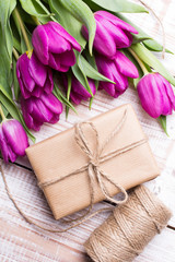 Fototapeta na wymiar Gift box and tulips bouquet on white wooden background - retro style