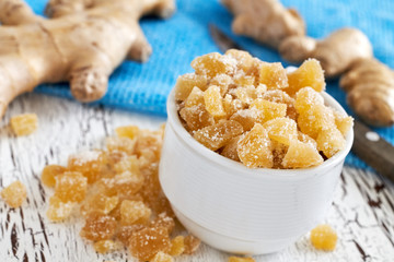 Candied ginger in cup on white rustic wooden background