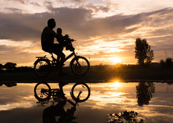 Fototapeta na wymiar Reflection Silhouette of Father with his toddler on bicycle agai