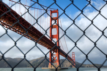 Obraz premium Golden Gate Bridge in San Francisco on a partly cloudy day behind a chain link fence