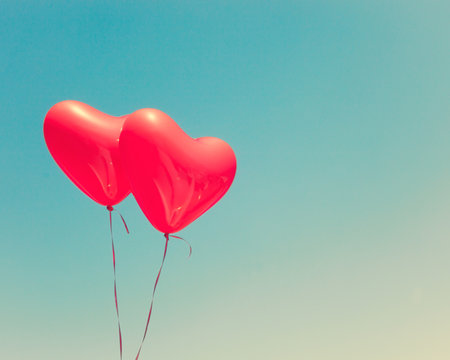 Two red heart shaped balloons in flight