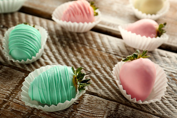 Strawberries covered with colorful chocolate icing on wooden background, closeup