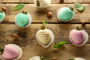 Strawberries covered with colorful chocolate icing on wooden background, closeup