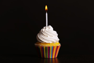 Fresh tasty cupcake with candle on dark background