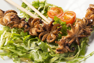 Barbecue baby octopus on white plate with herbs, tomatoes and sticks