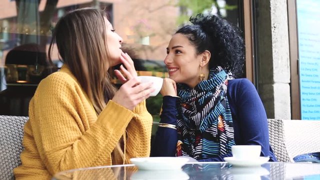 Lesbian couple at a cafe. Two young women are having a coffee together, talking, cuddling and give each other a kiss. Candid situation with real people. Homosexuality and lifestyle concepts.