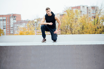 Portrait of a confident fitness guy. Man poses on skate ramp, against the background the city.