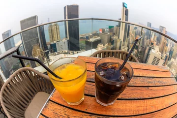 Wandcirkels tuinposter cocktail with city skyline view at dusk from skybar. fisheye angle of coke and juice close up. © bennymarty