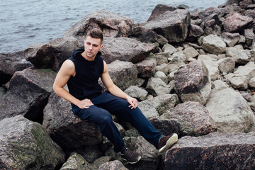 Strong yang fitness man poses on beach near sea and rocks.