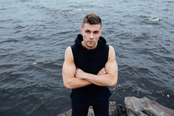 Strong yang fitness man poses on beach near sea and rocks.