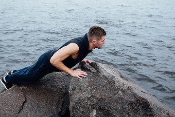 Strong man acts yoga on the rocks beach in the morning against sea.