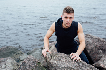 Strong man acts yoga on the rocks beach in the morning against sea.