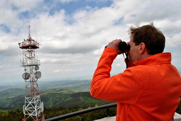 Mężczyzna spoglądający przez lornetkę na maszt antenowy