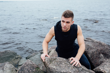 Strong man acts yoga on the rocks beach in the morning against sea.