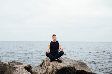 Fototapeta na wymiar Strong fitness yoga man in lotus pose on the rock beach near the ocean. Harmonic concept.