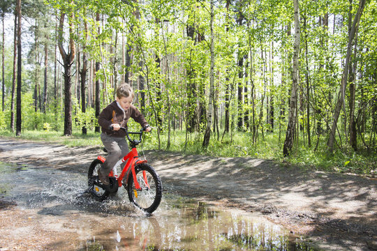 In the summer in the woods a little boy rides through a puddle o
