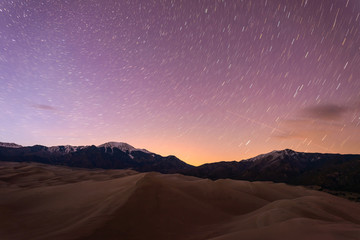 Starry Night at Great Sand Dunes - Star trails of spring night sky over snow peaks and great sand...