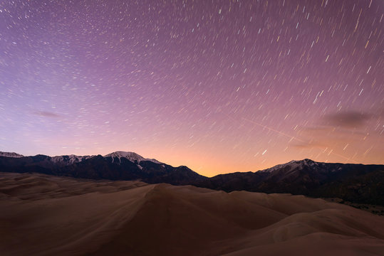 Starry Night At Great Sand Dunes - Star Trails Of Spring Night Sky Over Snow Peaks And Great Sand Dunes At Great Sand Dunes National Park & Preserve, Colorado, USA.