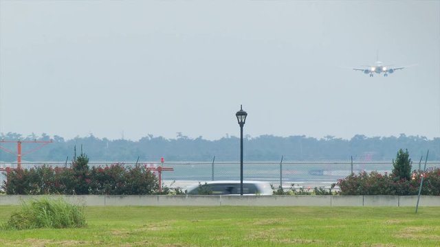 Runway Front View of Airliner on Final Approach Landing at Louis Armstrong New Orleans International Airport MSY with Vehicle Traffic Passing in Foreground