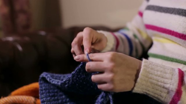 A woman crocheting on the couch. Female's hands knitting woolen threads.