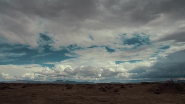 Time lapse storm clouds travel over a desert plain.