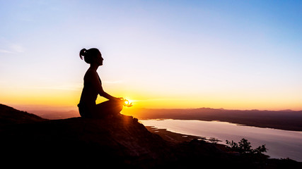Silhouette woman with yoga posture on the mountain at sunset.