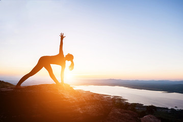 The woman with yoga posture on the mountain at sunset.