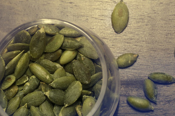 Pumpkin seeds in the glass bowl over wooden background close up