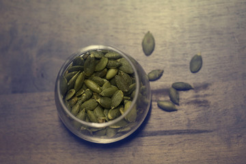 Pumpkin seeds in the glass bowl over wooden background close up