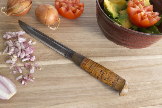 Wooden cutting board with knife, fresh onions, tomatoes and avocado