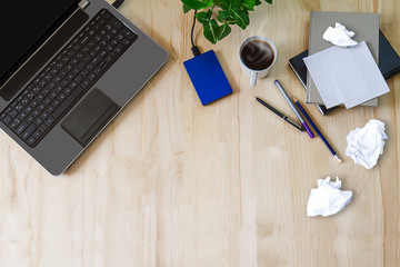 Laptop with office supplies, crumpled paper, green plant and hot black coffee with smoke on vintage...