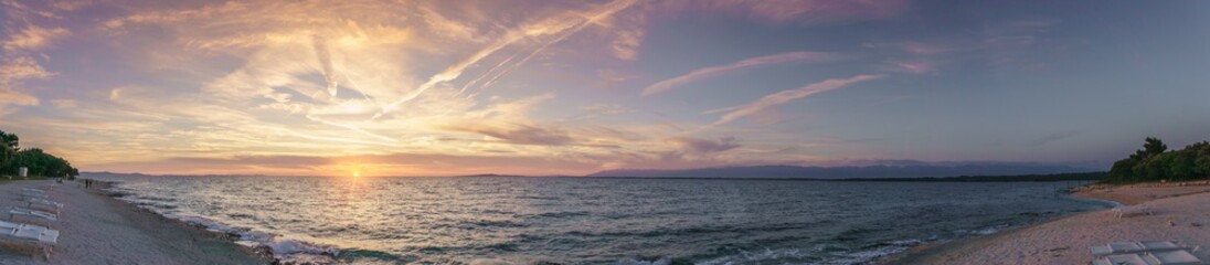 A panorama of the idyllic beach at the town of Petrcane, near Zadar, a town that lies on the Adriatic Sea in Croatia, as the setting sun sinks beneath the horizon.